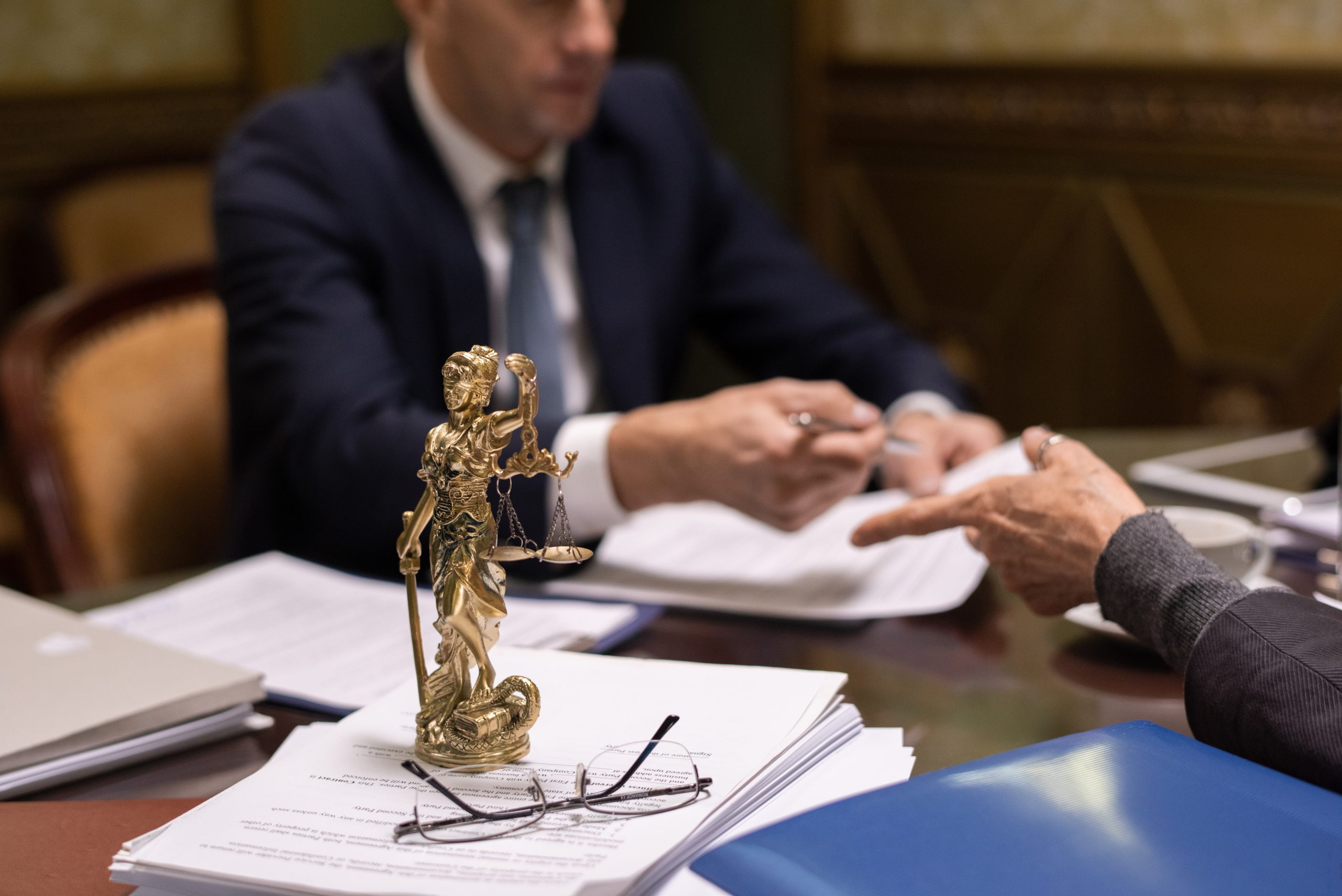Statue of justice and eyeglasses on stack of juridical papers on table where two lawyers discussing documents
