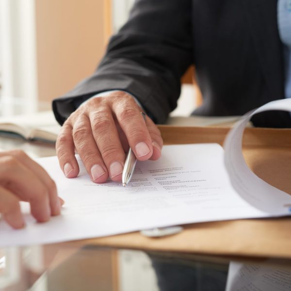 Close-up of businessman examining business contract and signing it at the office desk